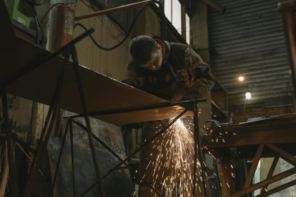 A worker focused on welding metal inside an industrial setting with sparks flying.